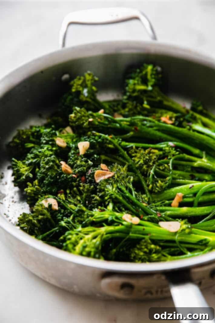 A close-up of tender sautéed broccolini in a pan, beautifully cooked with garlic chips and a hint of red pepper flakes.