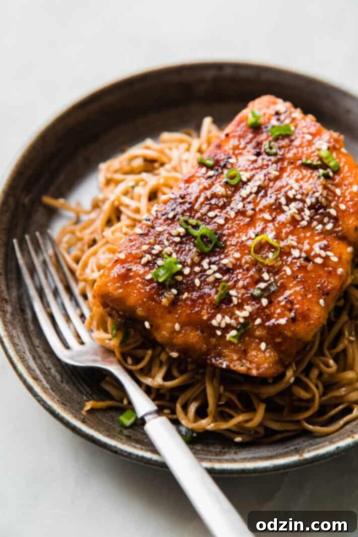 Sticky Teriyaki Salmon with Ginger Noodles 2 Buttery Teriyaki Sesame Salmon fillet resting on a generous portion of pan-fried ginger noodles, garnished with fresh green onions and sesame seeds.