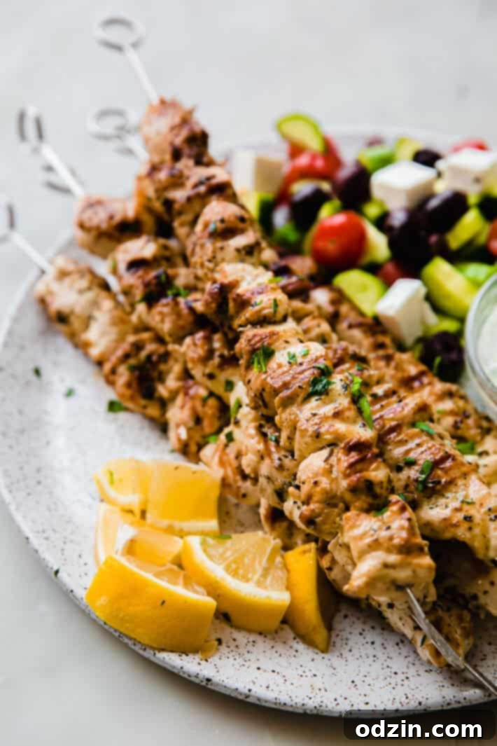 Zesty Greek Chicken Souvlaki Skewers 6 chicken souvlaki skewers on plate with lemons and greek salad