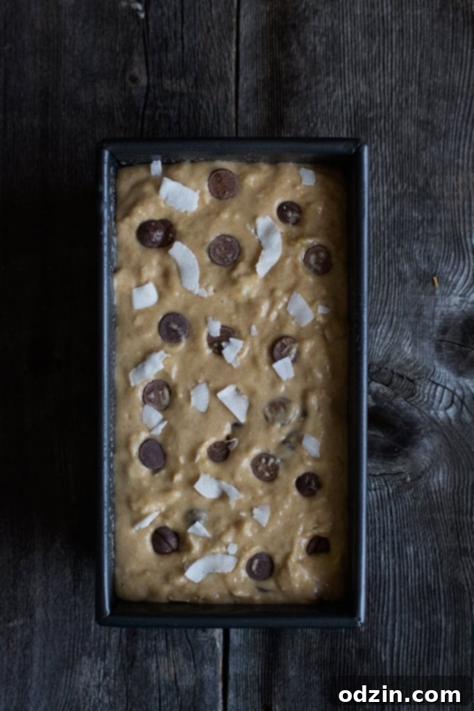 A slice of Coconut Chocolate Chip Banana Bread on a cooling rack, showcasing its moist texture and abundant chocolate and coconut pieces. #homemade #bakinglove