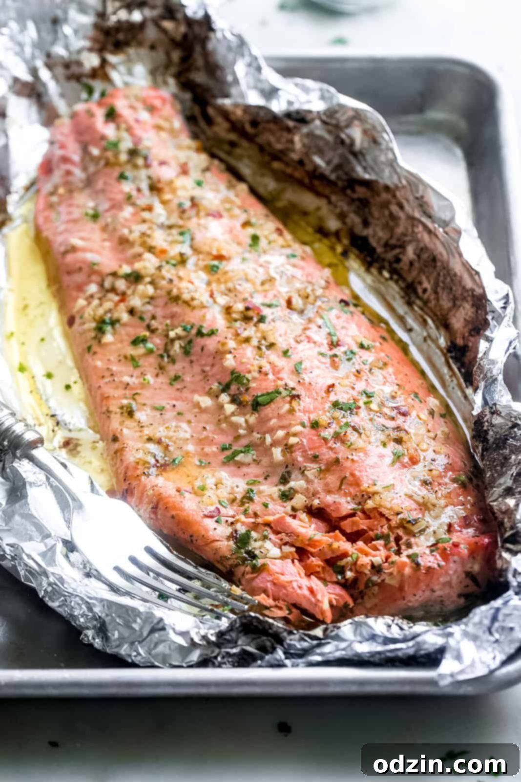 salmon filet prepared in foil with lemon garlic butter sauce drizzled on top
