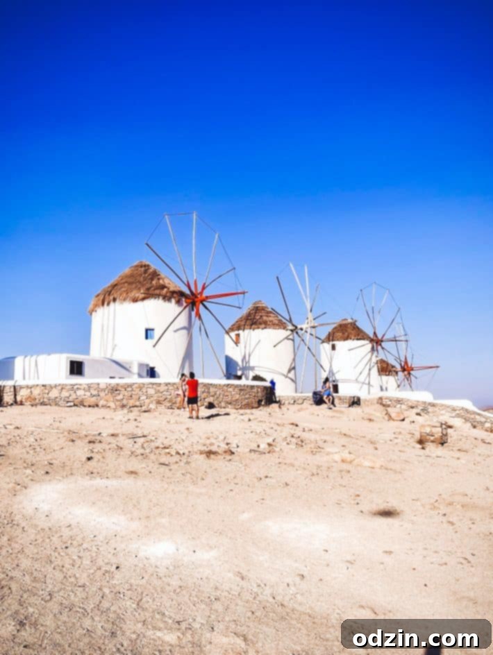 Iconic windmills of Mykonos silhouetted against a vibrant sunset sky