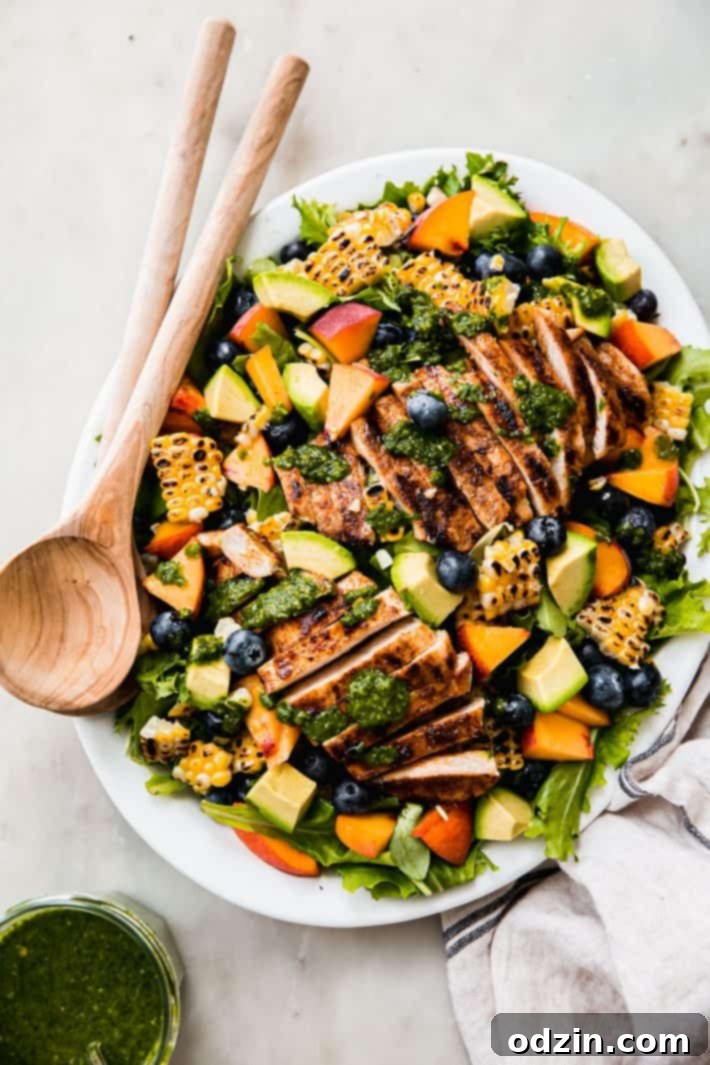 Platter displaying artfully arranged sliced chicken, fresh herb vinaigrette, peaches, avocado, grilled corn, and blueberries