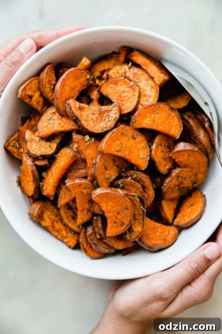 A bowl of roasted sweet potatoes, perfectly cooked and ready to serve, with a serving spoon.