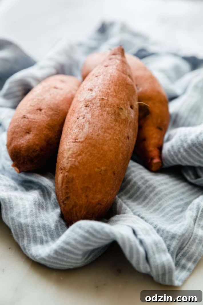 Fresh, whole sweet potatoes resting on a white tea towel, ready for preparation.