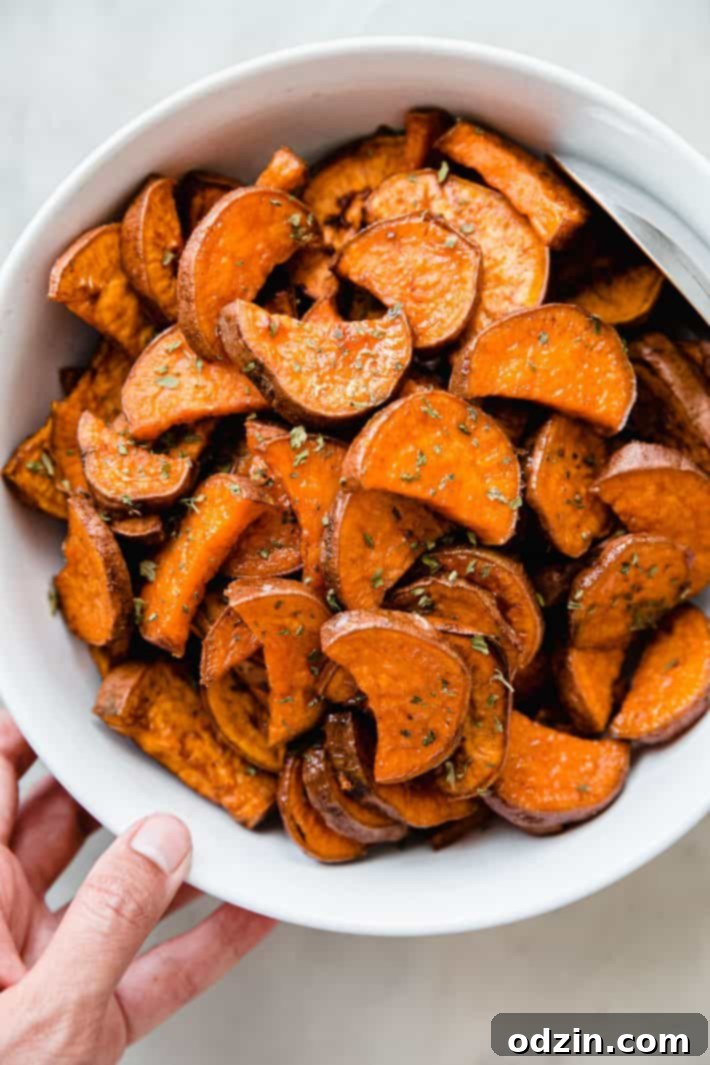 A bowl of roasted sweet potatoes, beautifully golden and garnished with dried parsley.