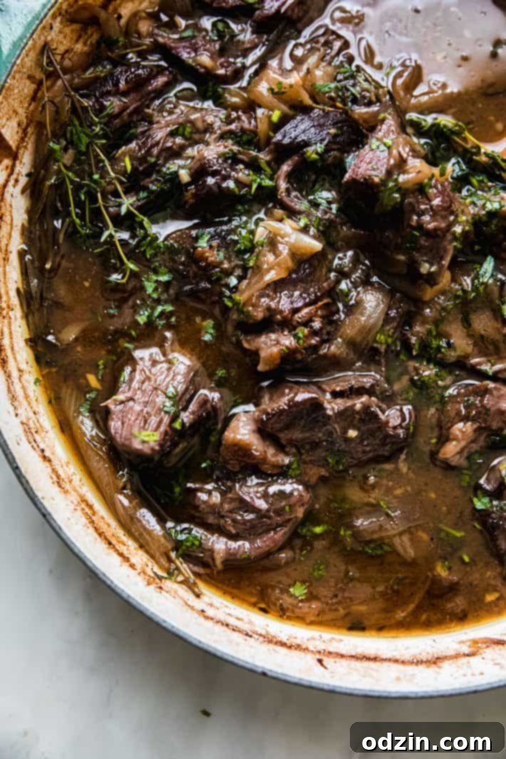Shredded tender beef sitting in a rich, glistening pan gravy after a long braise.