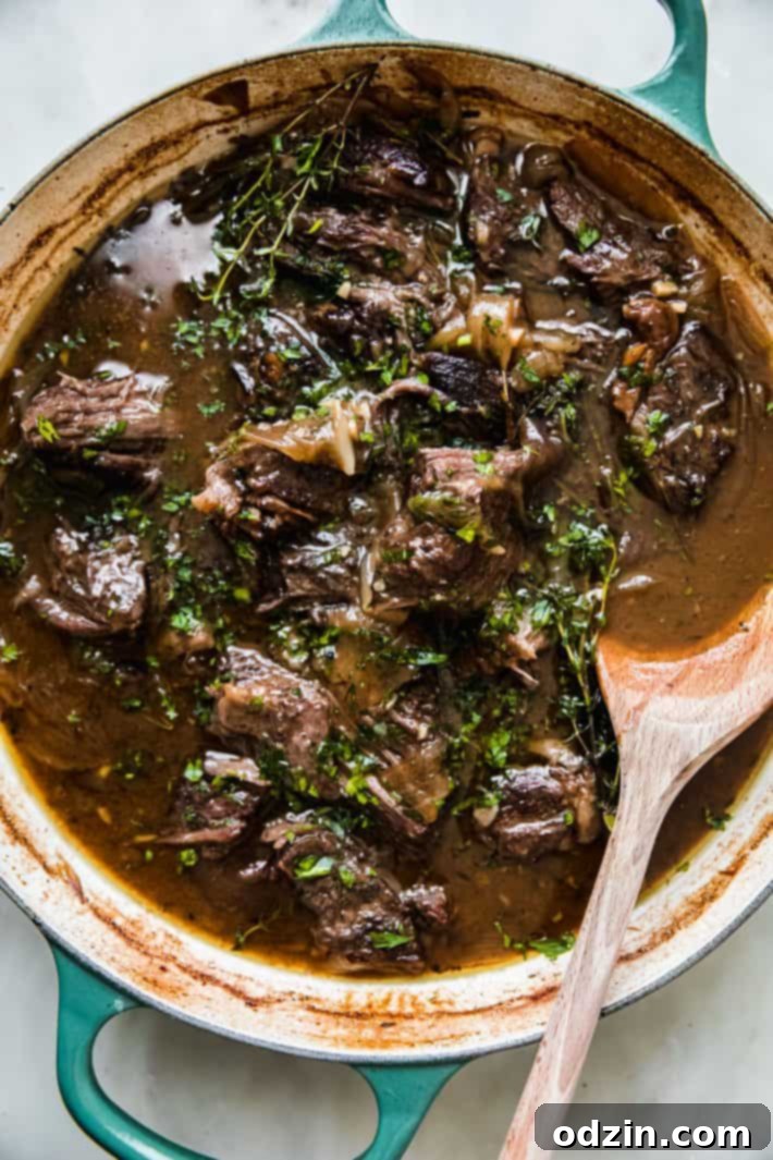Tender braised beef simmering in a Dutch oven with a wooden spoon, showcasing its rich, dark gravy.