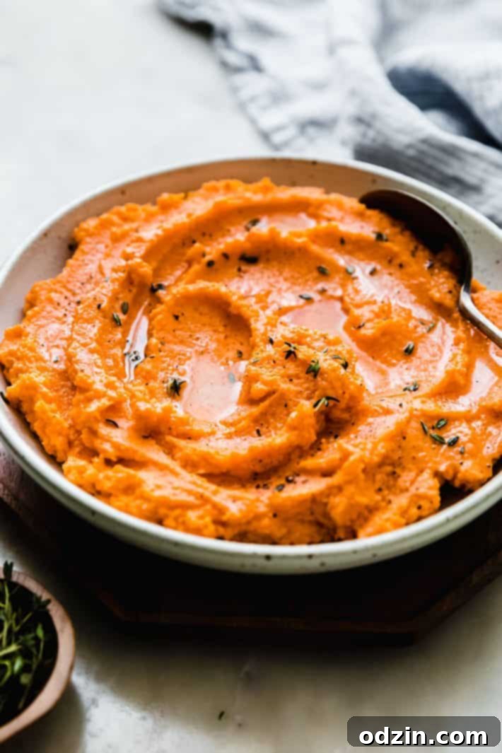 Close-up of fluffy mashed sweet potatoes in a bowl, garnished with butter and fresh thyme