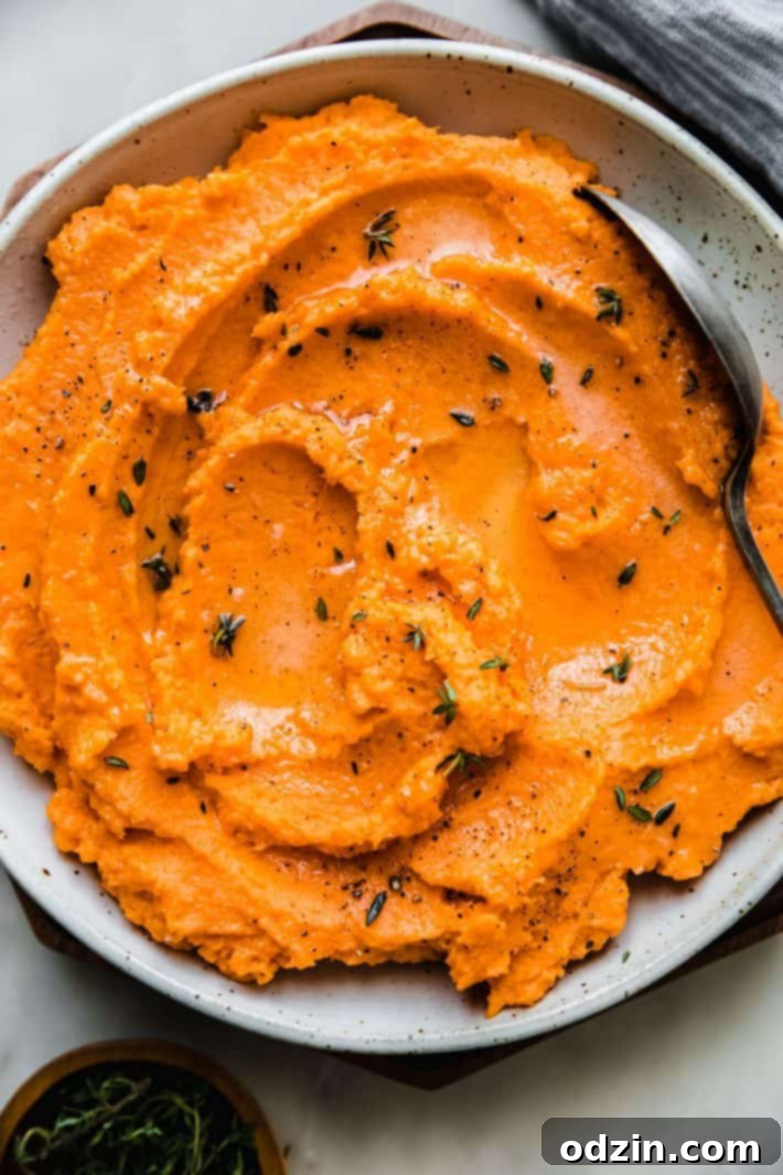 A serving of creamy sweet potato mash in a white dish, garnished with a spoon for serving