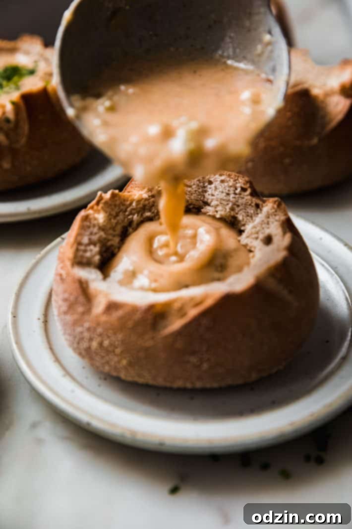 ladling gouda soup into bread bowl, illustrating the creamy texture and rich color of the soup