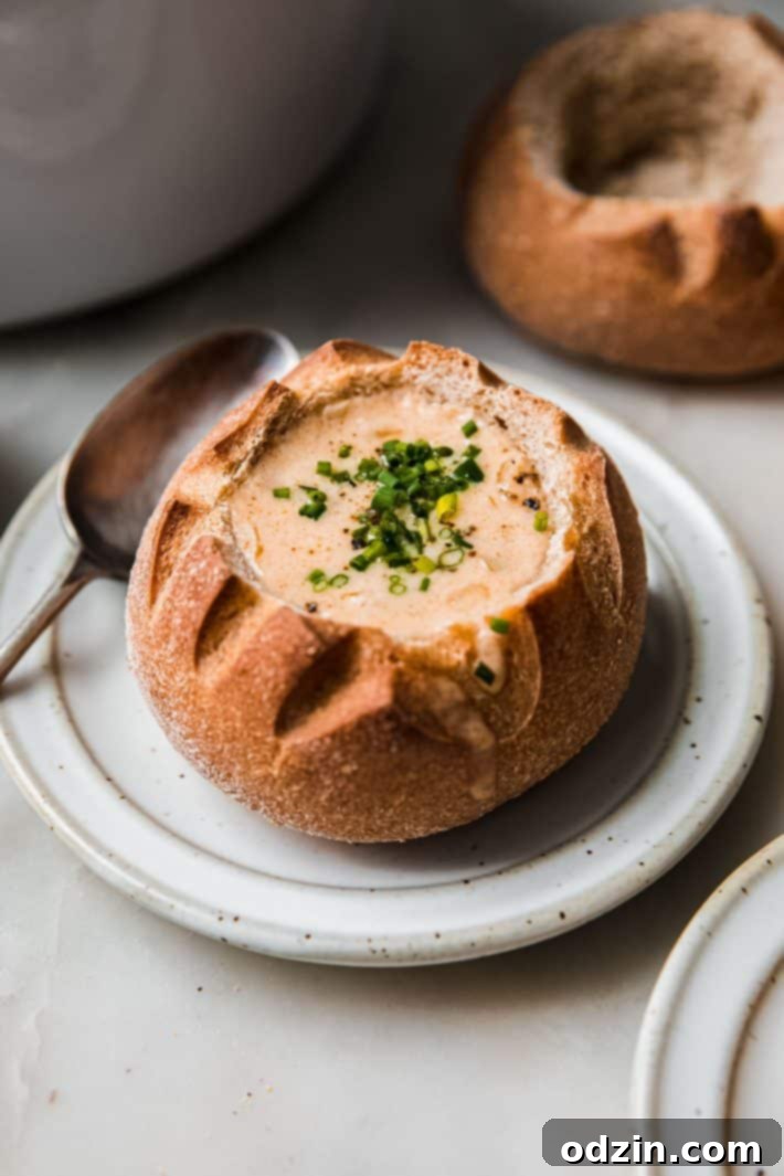 soup in bread bowl topped with chives on a plate with spoon, ready to be enjoyed