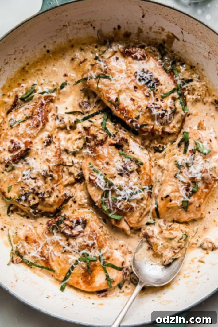 The Ultimate Marry Me Chicken Recipe 2 Delicious Marry Me Chicken served in a cast iron skillet with a spoon, highlighting its creamy sun-dried tomato and garlic sauce.