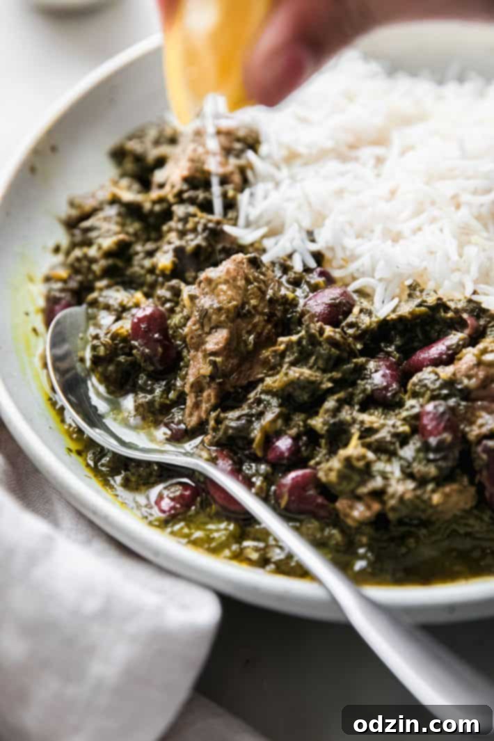 Fresh lemon being squeezed over a bowl of rich green Persian herb stew
