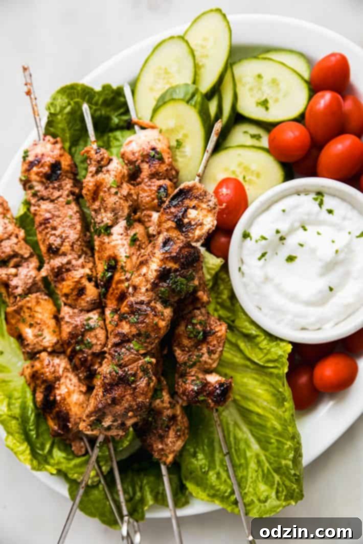 Platter of perfectly cooked chicken shish tawook skewers, served over a bed of fresh lettuce with a side of toum and grilled vegetables