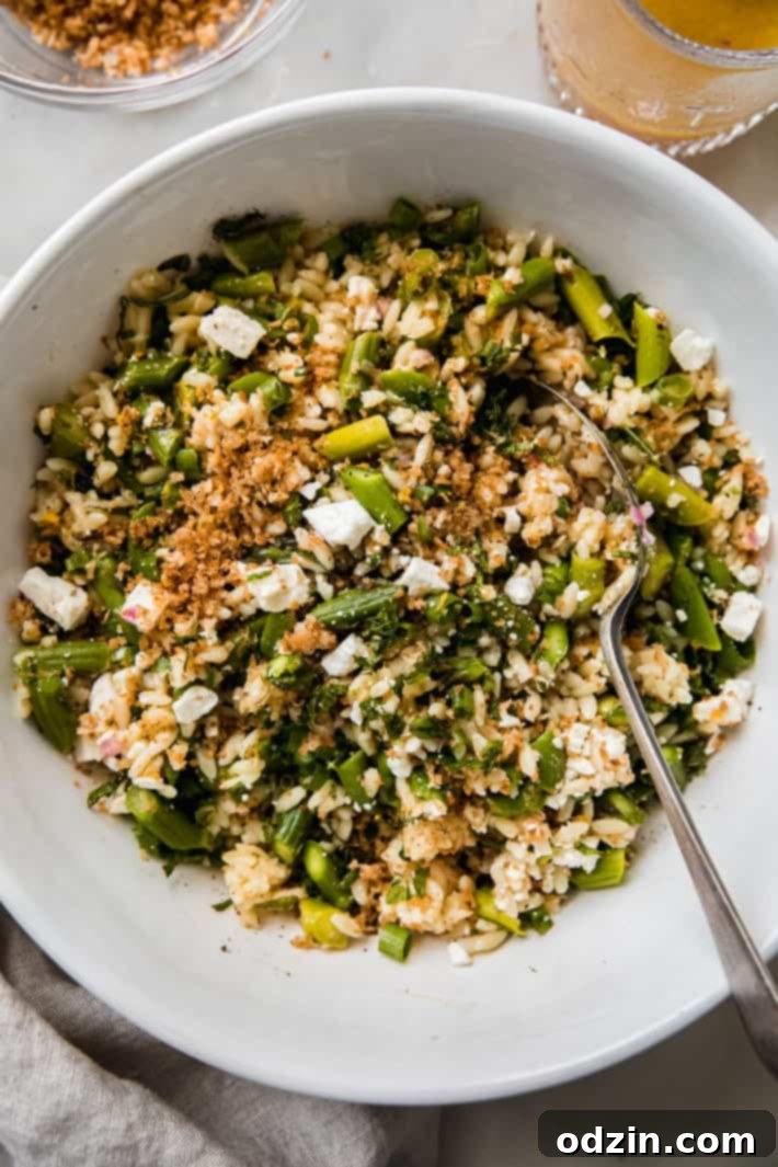 Large bowl of crunchy asparagus orzo salad with a spoon, ready to be served