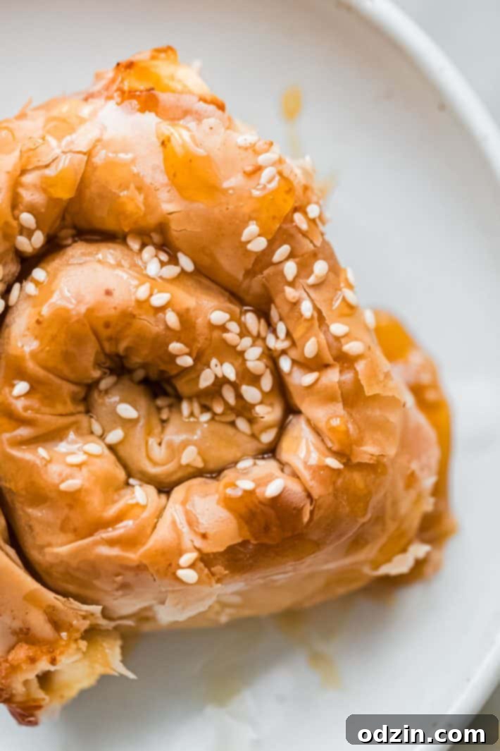 Golden phyllo wrapped feta cheese spirals on a white plate with a side of hot honey, ready to be served as an appetizer.
