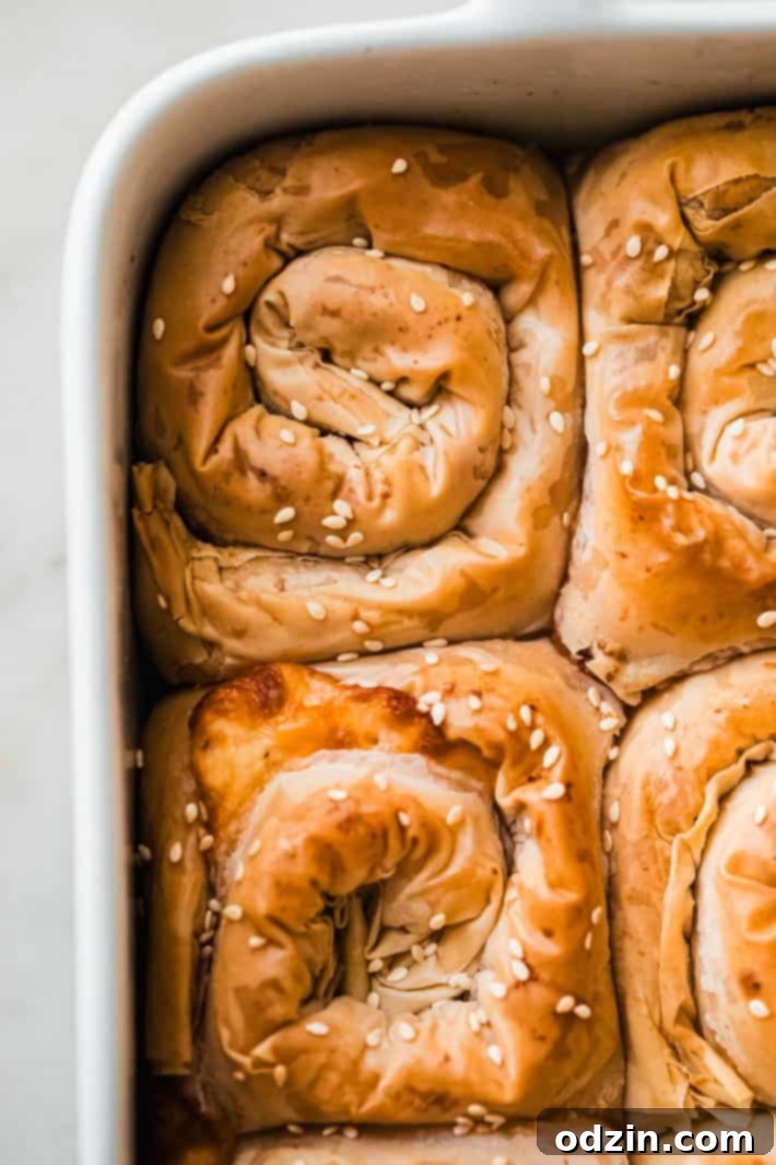 Crispy golden cheese spirals arranged in a round baking pan, generously sprinkled with sesame seeds, fresh from the oven.