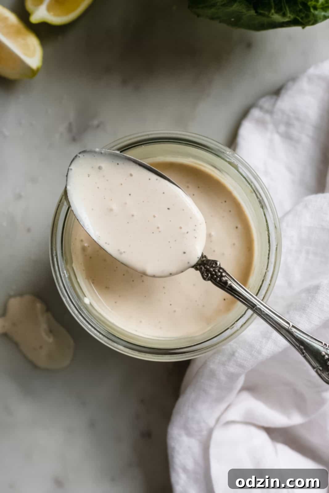 Caesar Dressing in 2 Minutes 3 Spoon holding creamy Caesar dressing, resting on a glass jar filled with the dressing