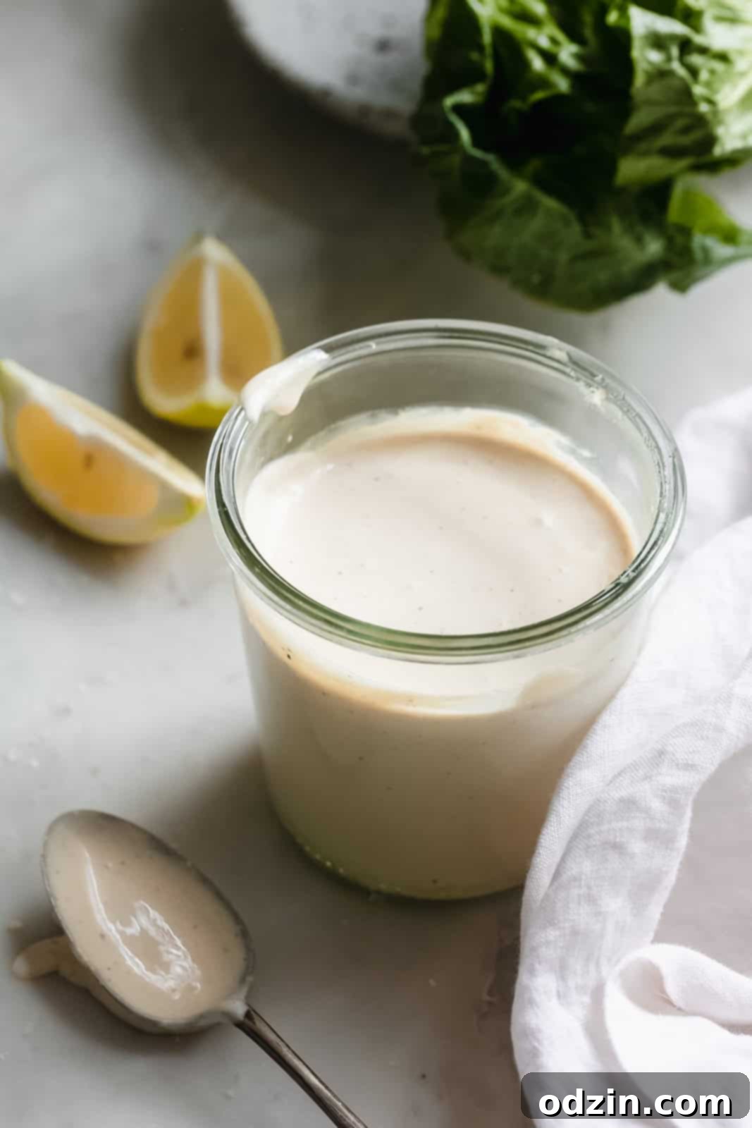 Caesar Dressing in 2 Minutes 5 Prepared Caesar dressing in a jar, surrounded by fresh lemon wedges, romaine lettuce, a tea towel, and a spoon