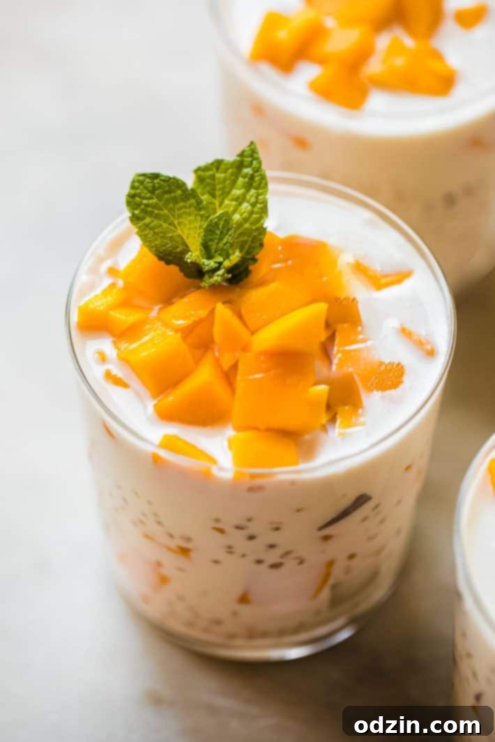 Mango Sago Dessert in a glass cup, garnished with fresh mango chunks and a sprig of mint, highlighting its creamy texture and vibrant color.