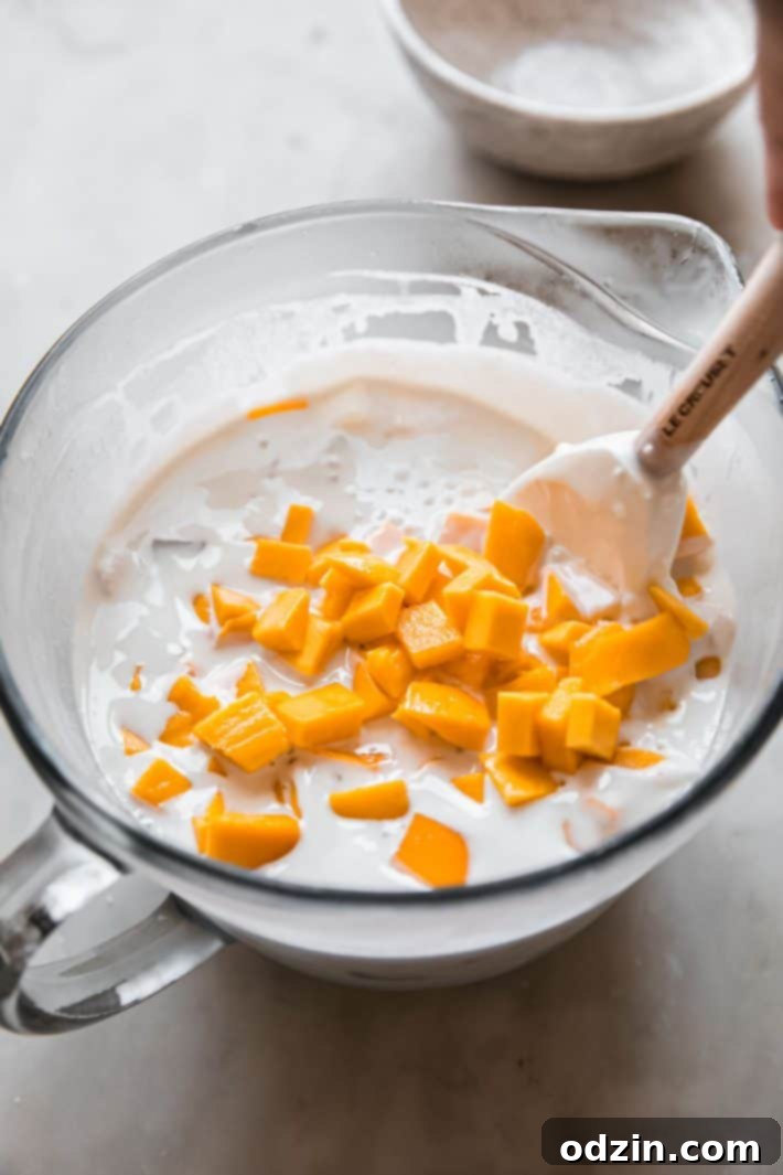 A glass measuring cup filled with creamy tapioca pudding, topped with generous mango chunks and a vintage Le Creuset stirring spoon, ready to be served.