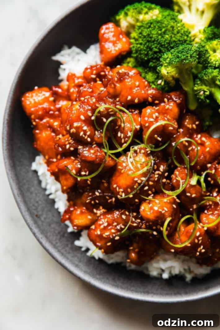 Garlic Gochujang Chicken in a bowl with white rice, steamed broccoli, sesame seeds, and green onions, ready to be served.