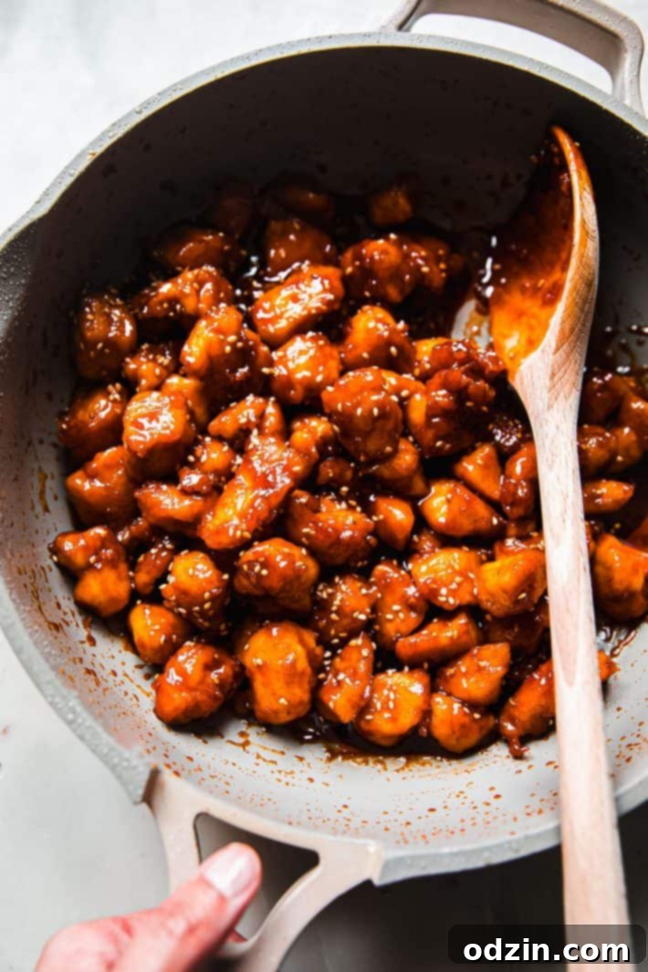 Crispy chicken tossed in a rich gochujang honey sauce in a large skillet with a wooden spoon, showcasing the delicious glaze.
