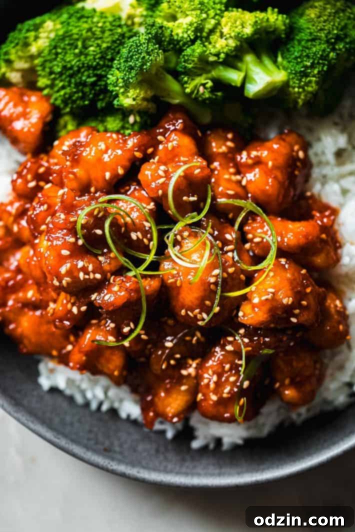 Gochujang chicken served over rice with steamed broccoli, garnished with fresh green onions and sesame seeds, ready to eat.