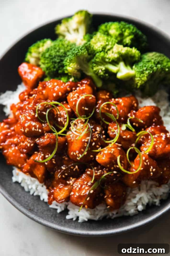 Prepared Gochujang chicken served in a bowl over rice with a side of steamed broccoli, garnished beautifully.