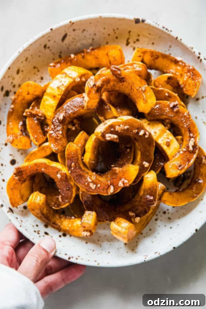 Close-up of golden-brown maple roasted delicata squash slices in a speckled ceramic bowl, ready to be served.