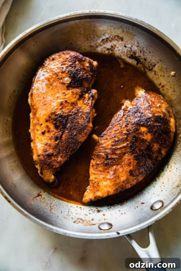 Close-up of blackened chicken searing in a hot skillet, ready for the harvest bowl