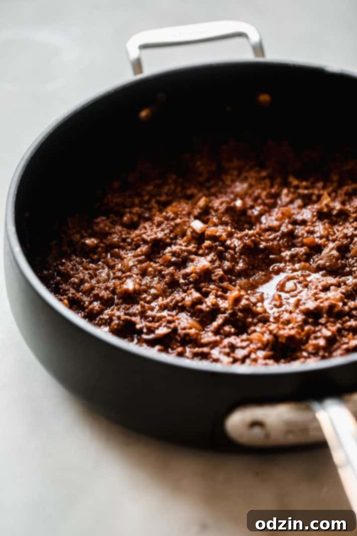 Egyptian Béchamel Macaroni Bake 4 A close-up shot of a savory ground beef and tomato meat sauce simmering in a large sauté pan, vibrant and rich in color.