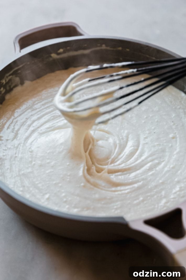 Egyptian Béchamel Macaroni Bake 5 A creamy, smooth béchamel sauce being whisked in a saucepan, showing its perfect consistency, with a whisk resting in the pan.