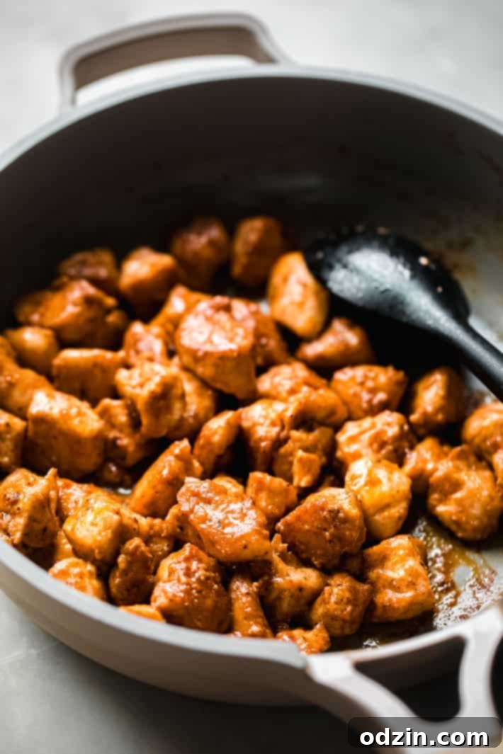 Cooked buffalo chicken simmering in a pan with sauce and a serving spoon