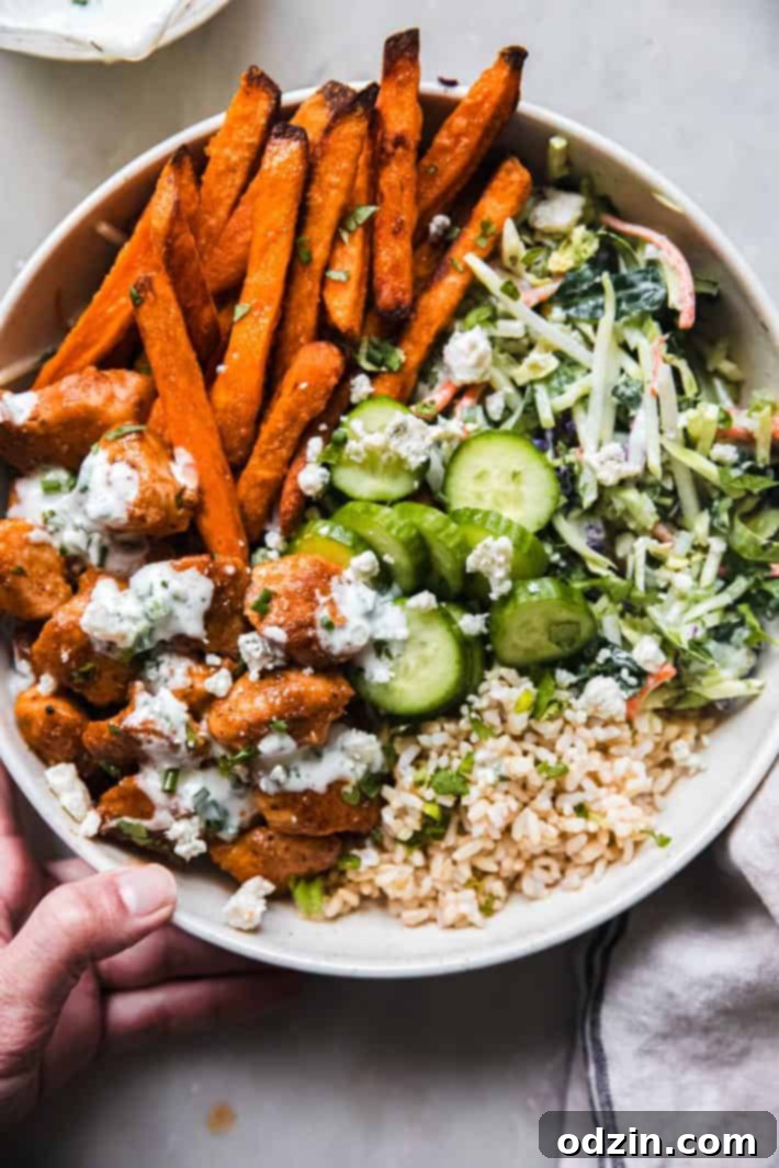 A completed buffalo chicken bowl, showcasing chicken in buffalo sauce, blue cheese, sweet potato fries, cucumber, rice, and slaw