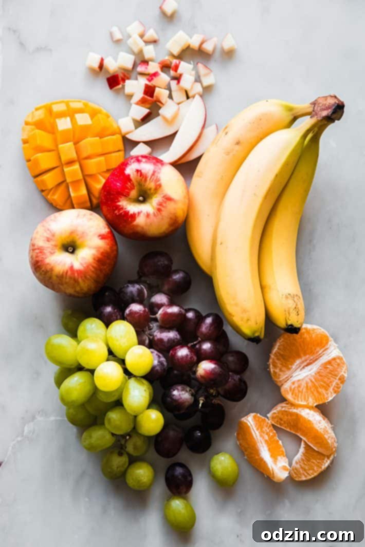 whole banana, apples, grapes and sliced mango and tangerines on marble