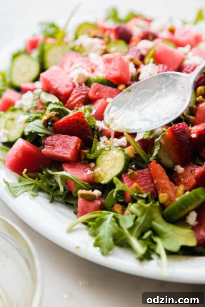 Close-up of a watermelon salad with lime dressing being drizzled over it, highlighting fresh ingredients