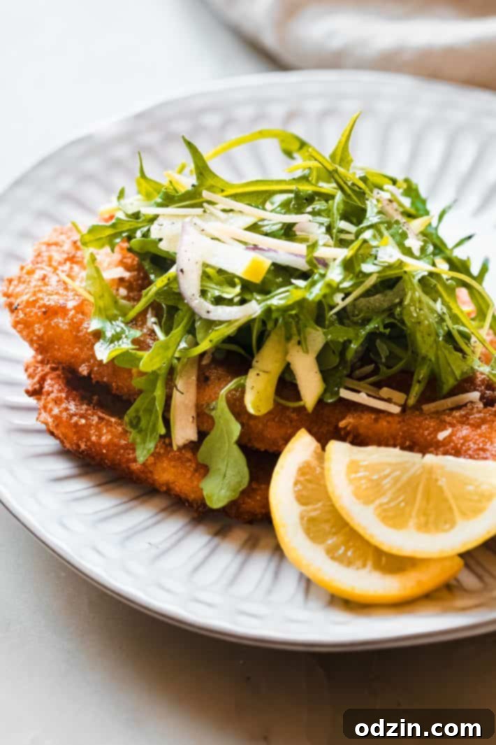 crusted chicken romano cutlet on plate with arugula salad on top, garnished with fresh herbs