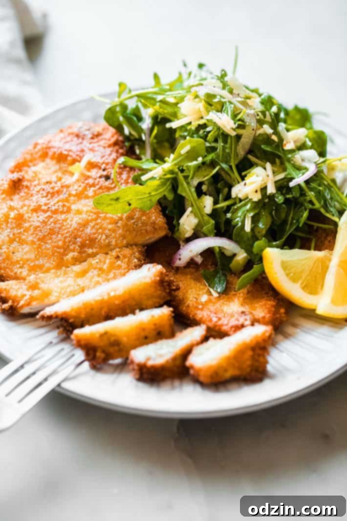 sliced romano chicken cutlets on plate with fresh arugula salad and lemon wedges