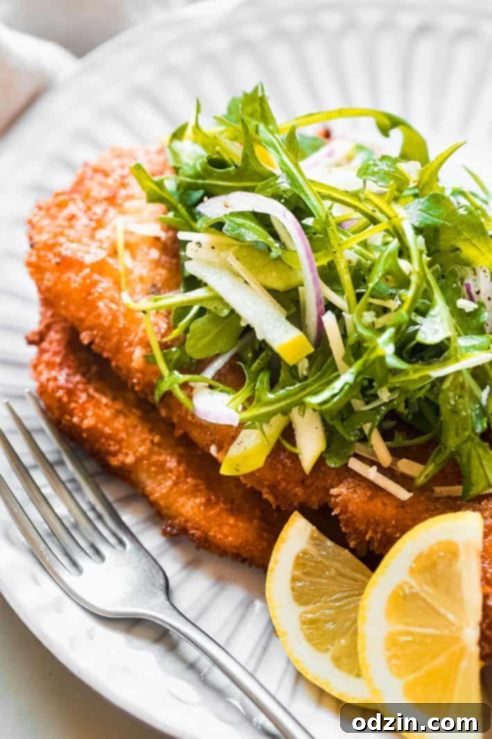 finished panko breaded chicken cutlets on plate with arugula salad and lemon wedges