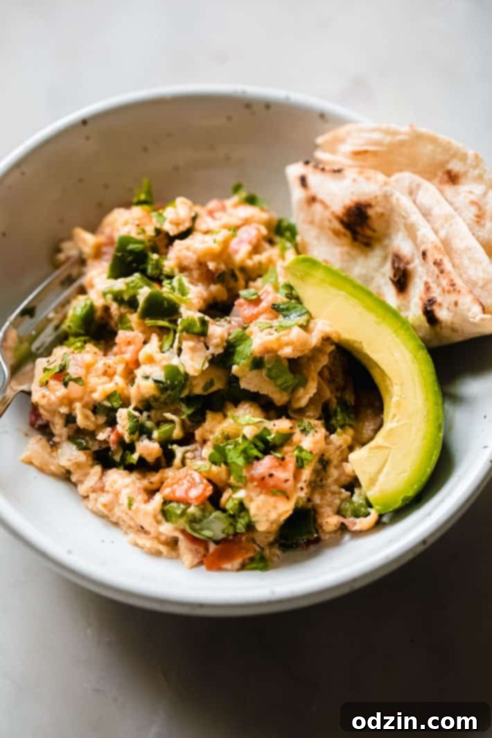 huevos a la mexicana in bowl with fork, avocado wedges, and tortilla