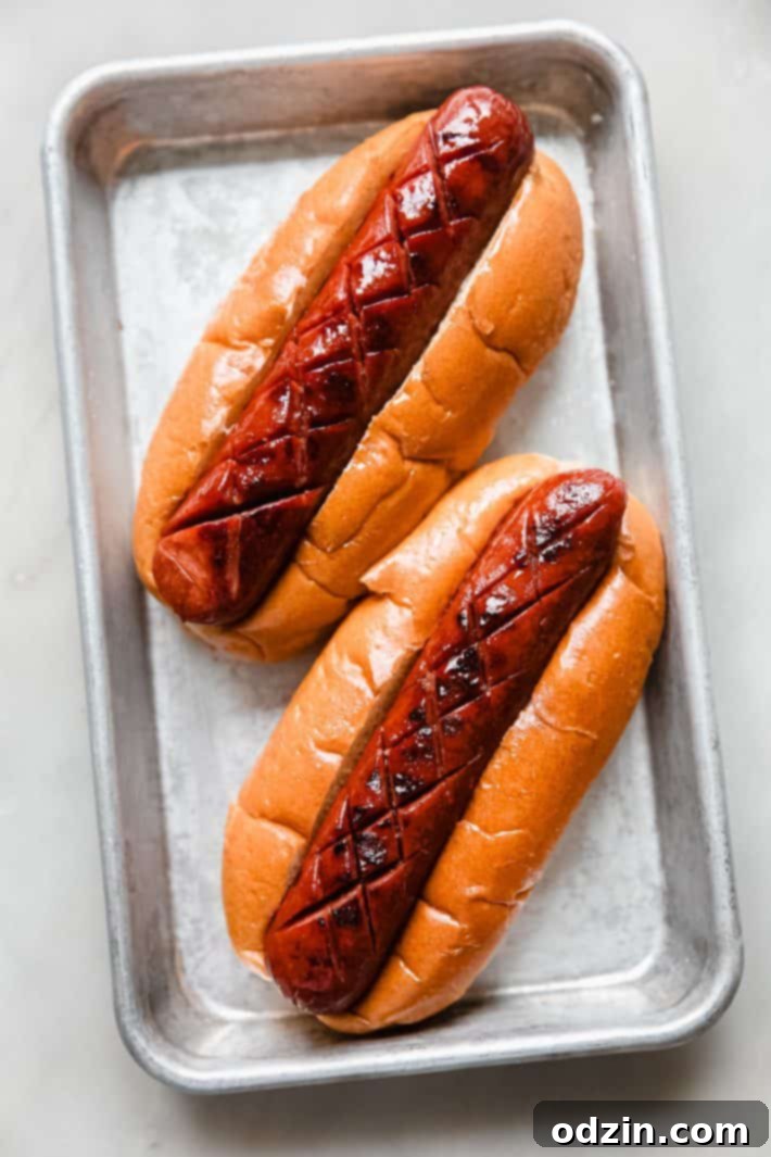 Cross-hatch marked hot dogs perfectly grilled and loaded into soft brioche hot dog buns on a metal pan