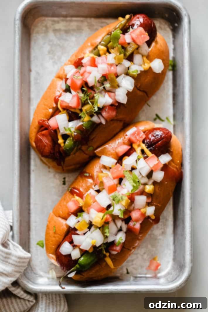 Prepared Mexican style hot dogs with pico de gallo and charred peppers on a metal pan, ready to serve