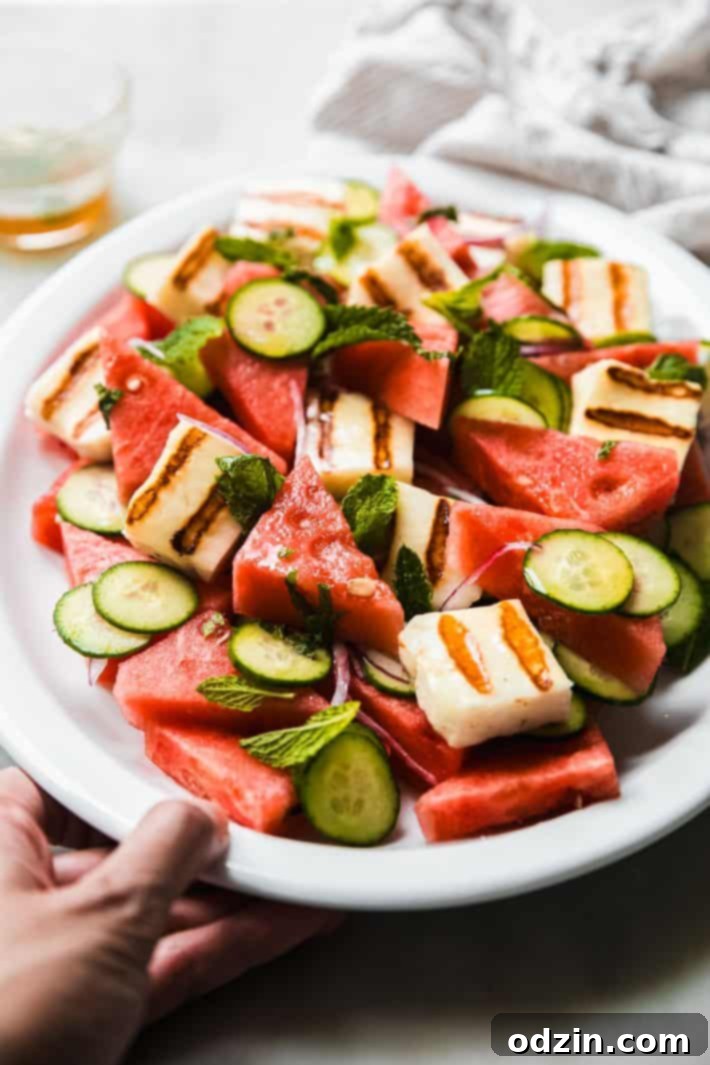 Grilled Halloumi Watermelon Salad served on a white plate with cucumber, fresh mint, and thinly sliced red onion garnish