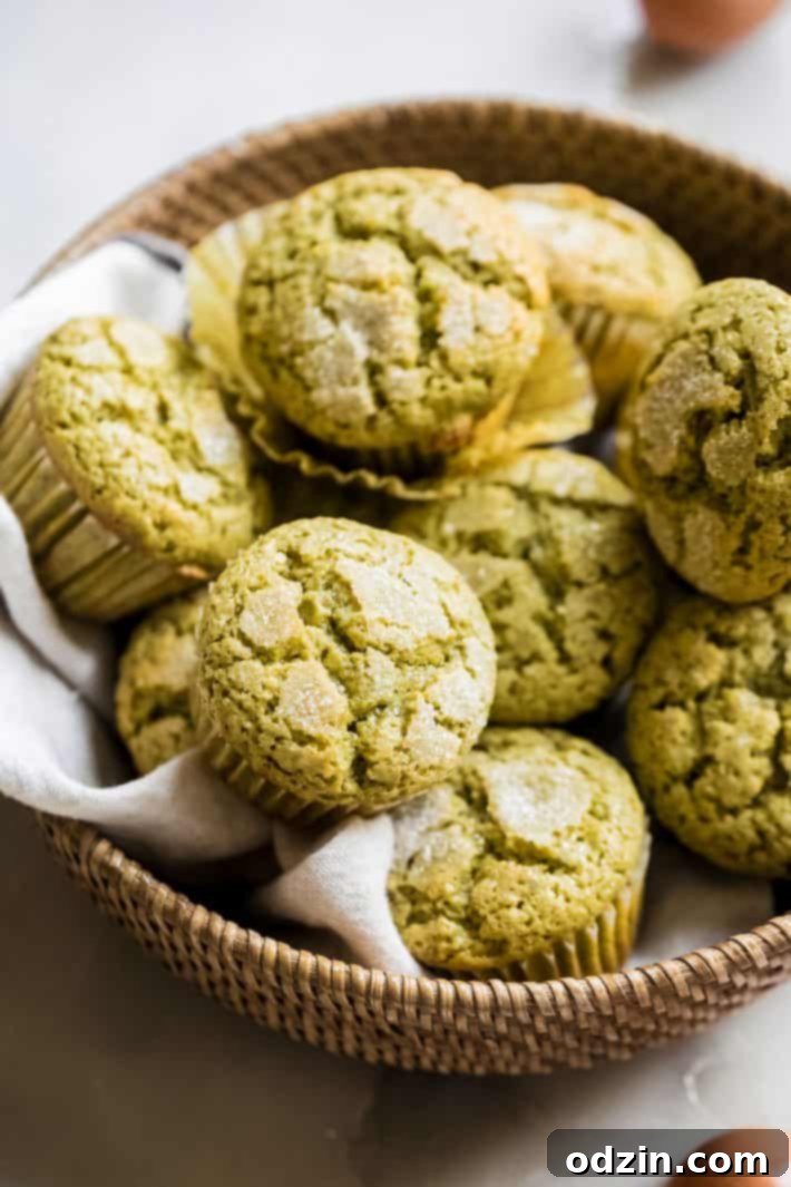 Perfectly Pistachio Muffins: Bakery Quality, Pudding-Free 2 Freshly baked pistachio muffins in a rustic basket, showcasing their perfect domed tops and a soft kitchen towel beside them.