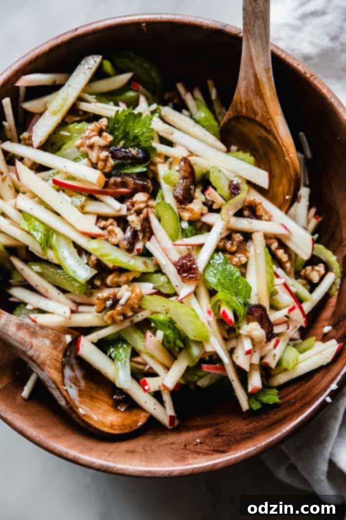 bowl of matchstick apple and celery salad with wooden spoons in wooden bowl