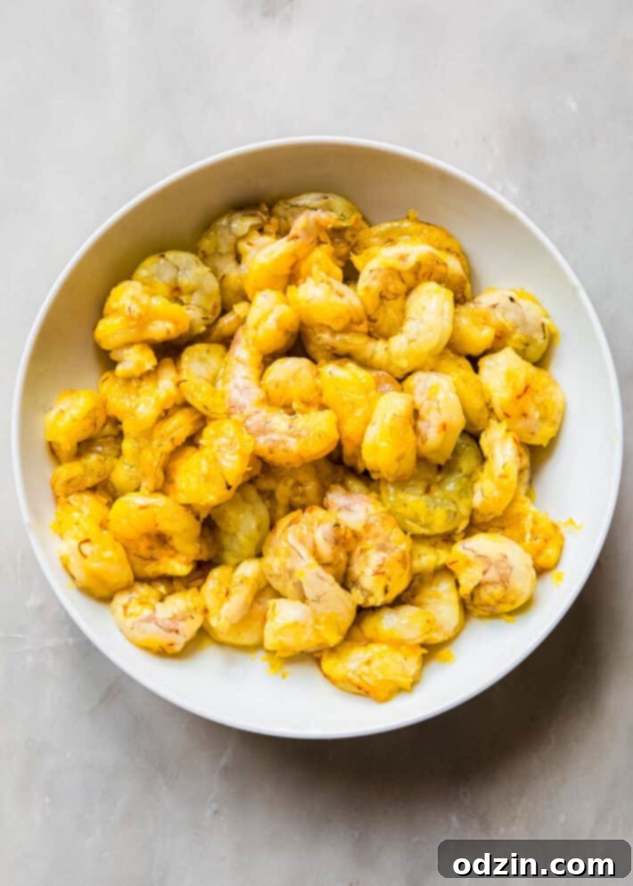 Shrimp marinating in a glass bowl with grated onions, saffron, and kosher salt, ready for cooking.