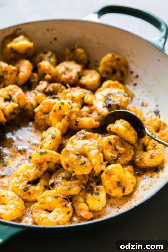 A serving spoon lifting cooked saffron shrimp from a cast iron pan, showing the rich sauce.