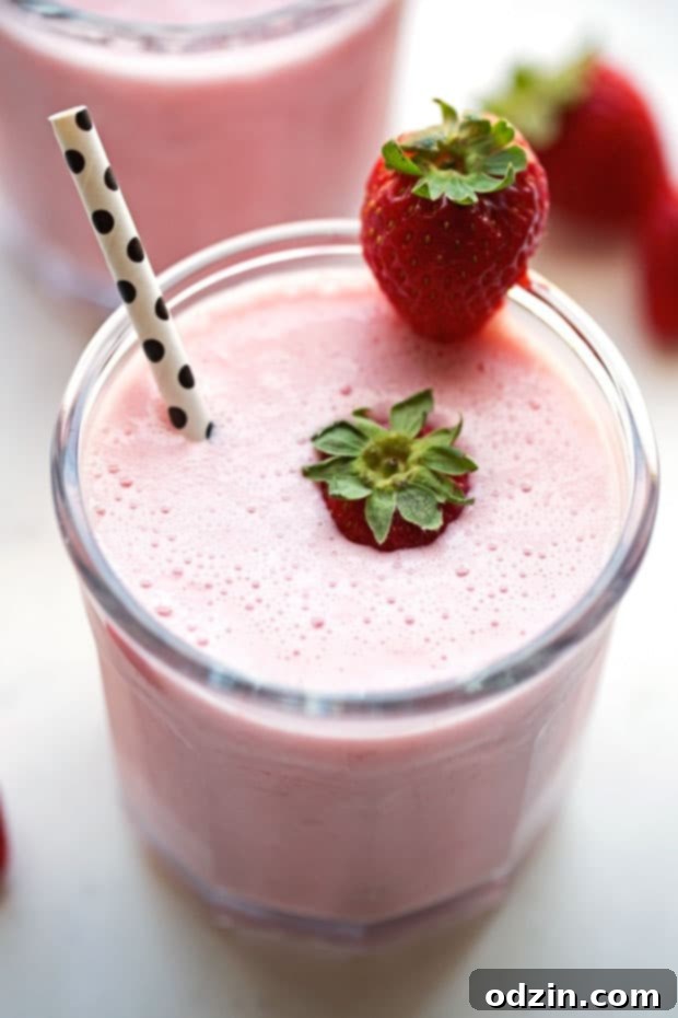 A tall, condensation-beaded glass of Strawberry Rose Lassi, garnished with a fresh strawberry slice and mint sprig, against a light backdrop. Evokes freshness and thirst-quenching qualities. Keywords: #refreshingdrink #strawberrylassi #healthychoice #drinkoftheday